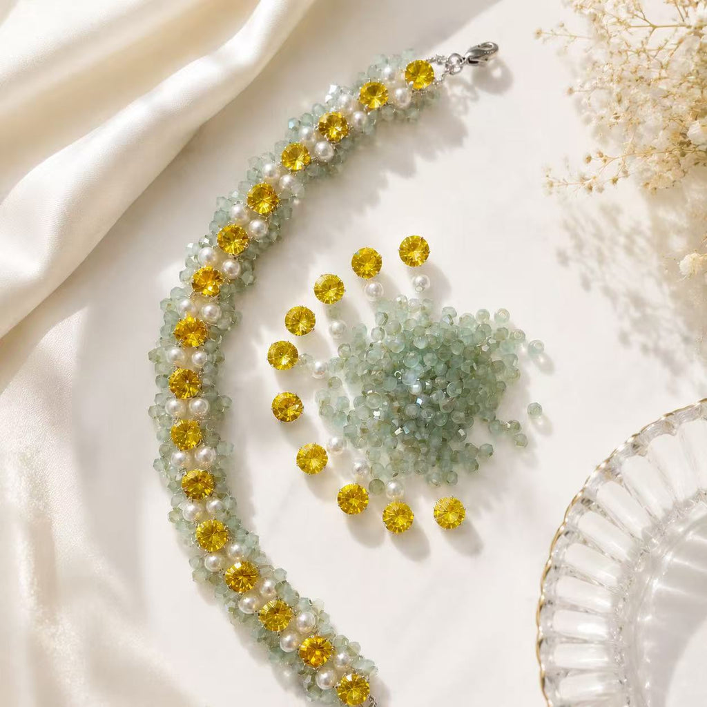 Lumière Weave Bracelet styled flat lay with golden crystals, ivory pearls and sage beads on white silk